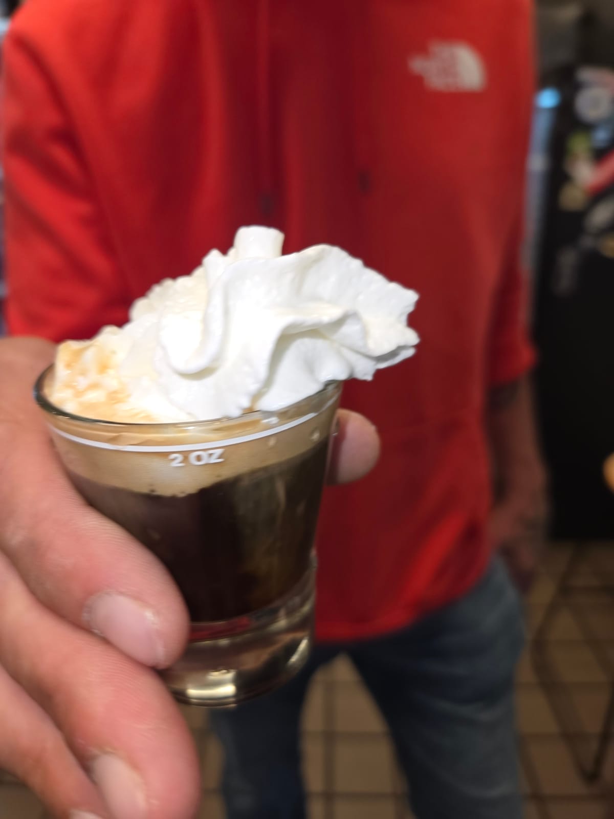 A Cafe Con Panna, a shot of espresso topped with a swirl of real whipped cream, held up in a small glass